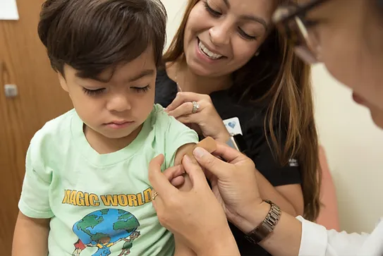 Young Hispanic boy receiving a band-aid after a vaccination while sitting on his mom's lap