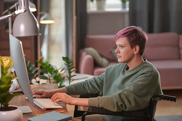 Teen with short pink hair typing at a desktop computer