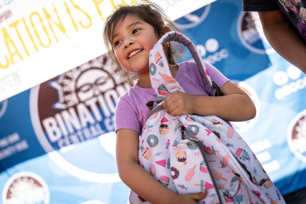 Little girl holding backpack at Binational California hub event.